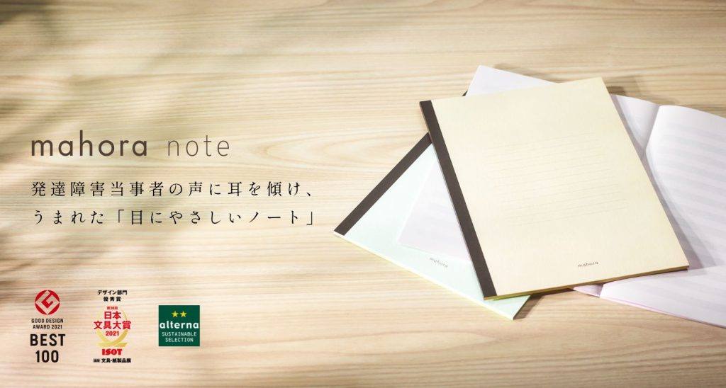 「mahora note」の広告画像。
木目調のデスクの上に、優しい色合いのノートが3冊並べられている。
キャッチコピーとして「発達障害当事者の声に耳を傾け、うまれた『目にやさしいノート』」と書かれており、視認性を重視したノートであることを伝えている。
左下には「GOOD DESIGN AWARD 2021」や「日本文具大賞」などの受賞歴が掲載され、品質の高さが強調されている。